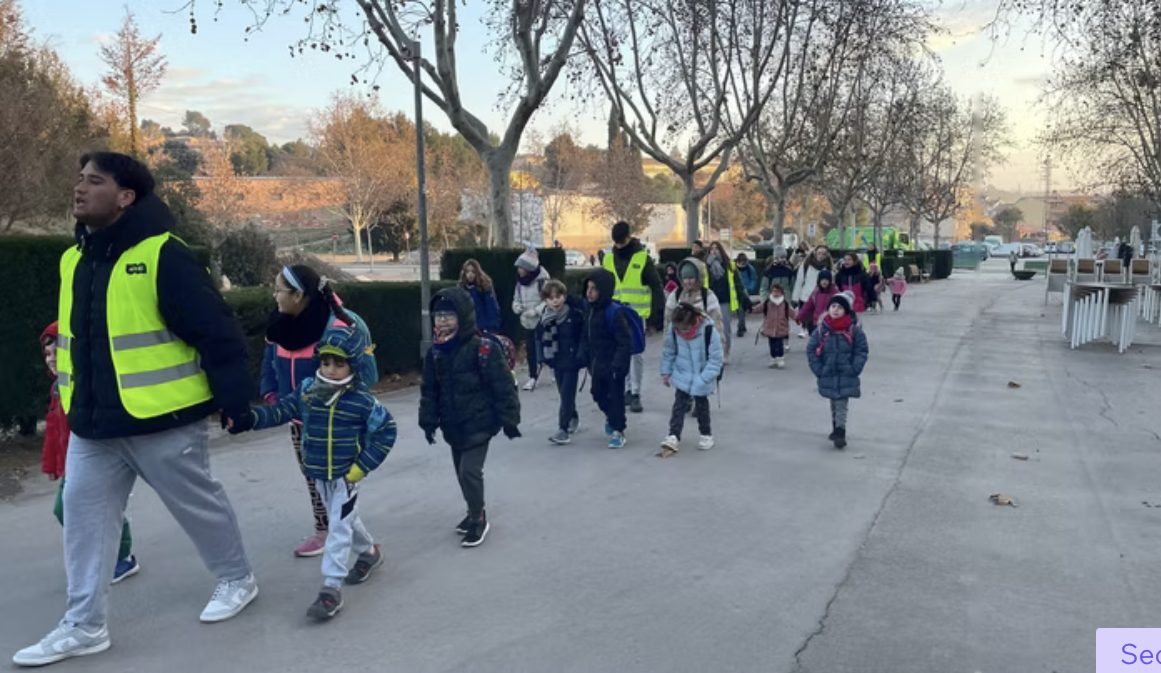 Monitor acompanyant un grup d'infants a peu per un passeig cap a l'escola